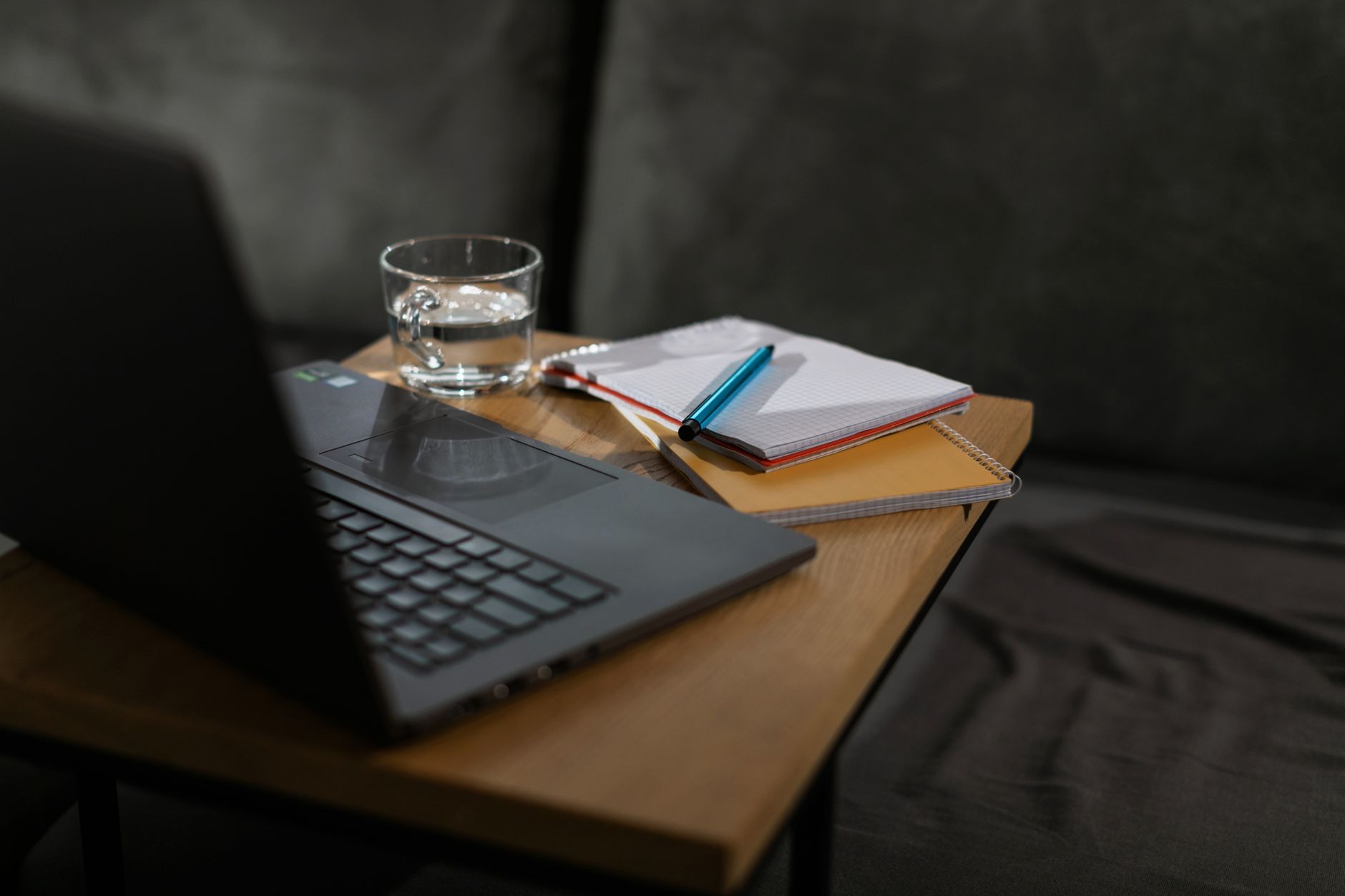 Minimalistische werkplek met laptop, notitieboeken en een glas water op een houten tafel.
