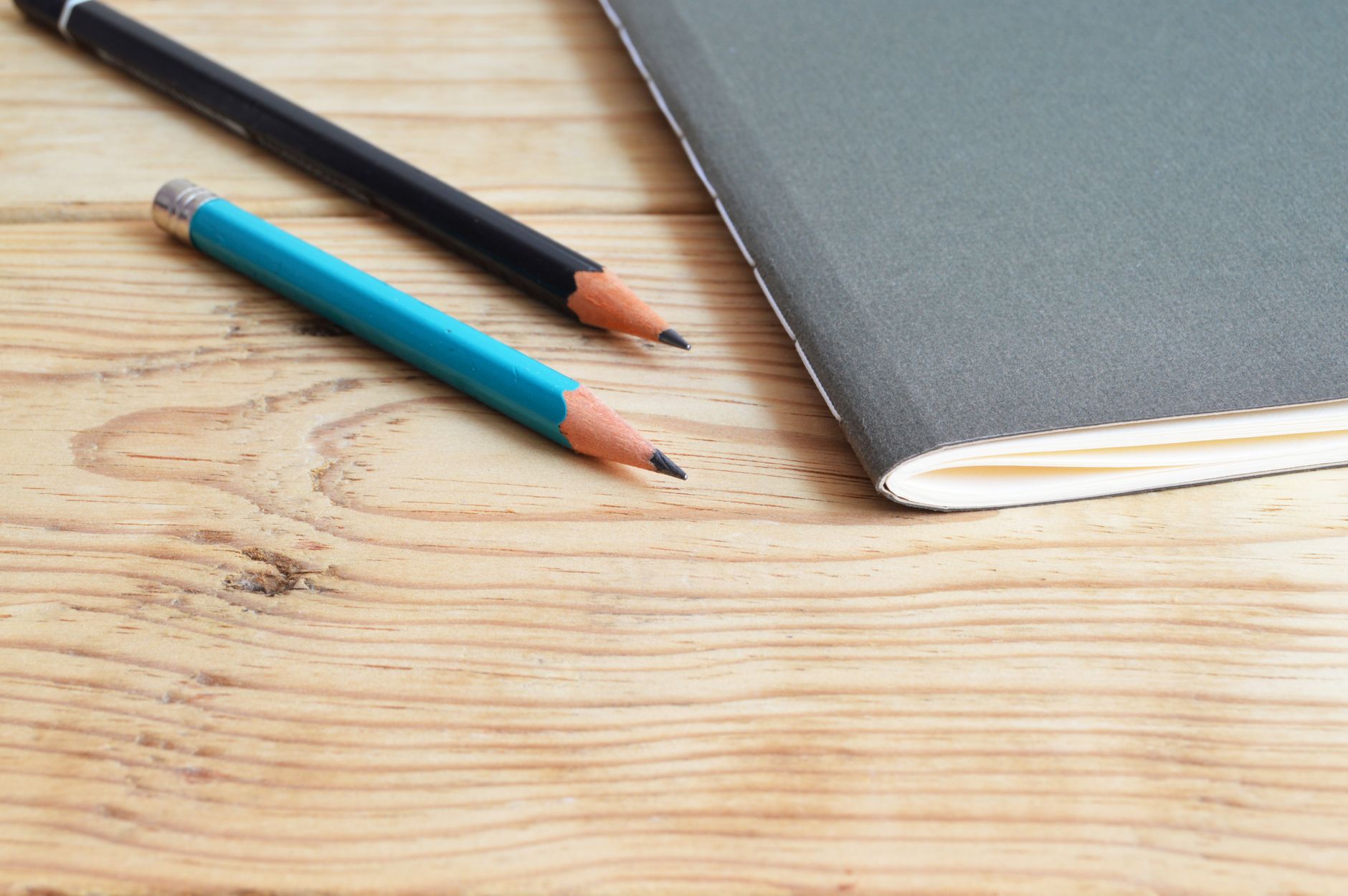 Minimalistische compositie van een notitieboek en potloden op een houten bureau.